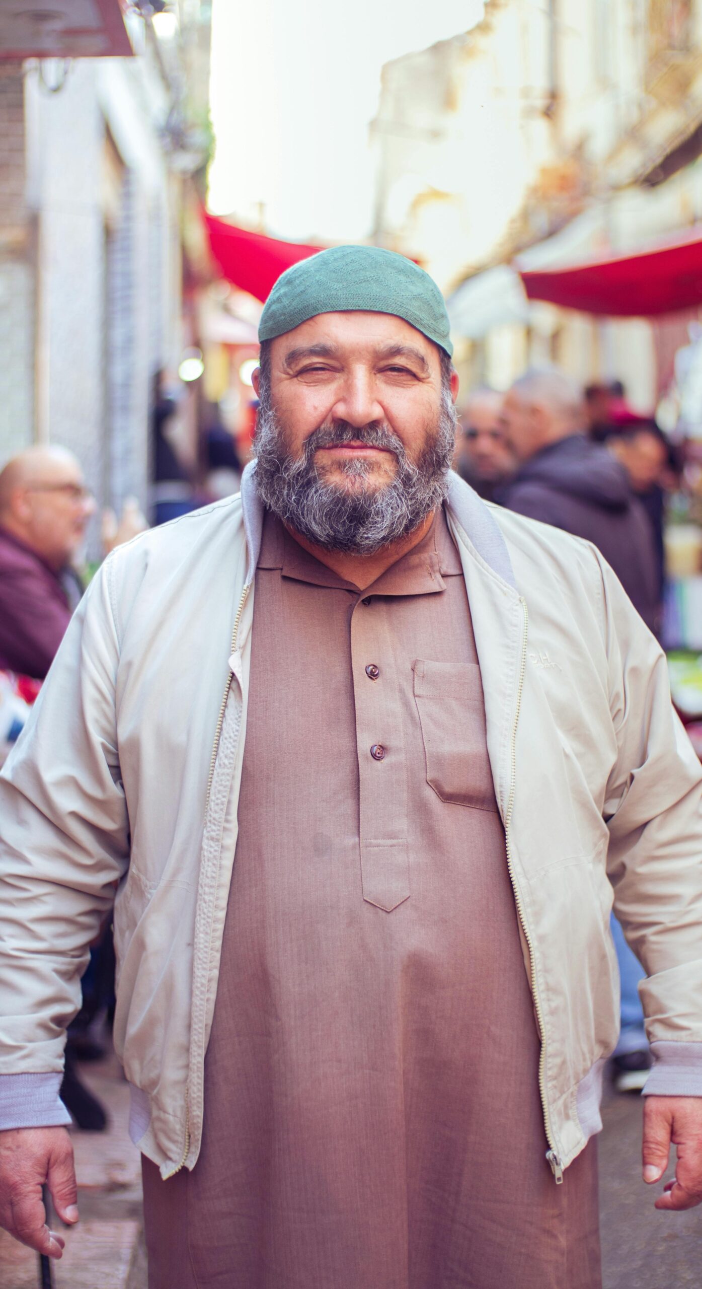 Smiling man in traditional clothing in a vibrant outdoor market setting.