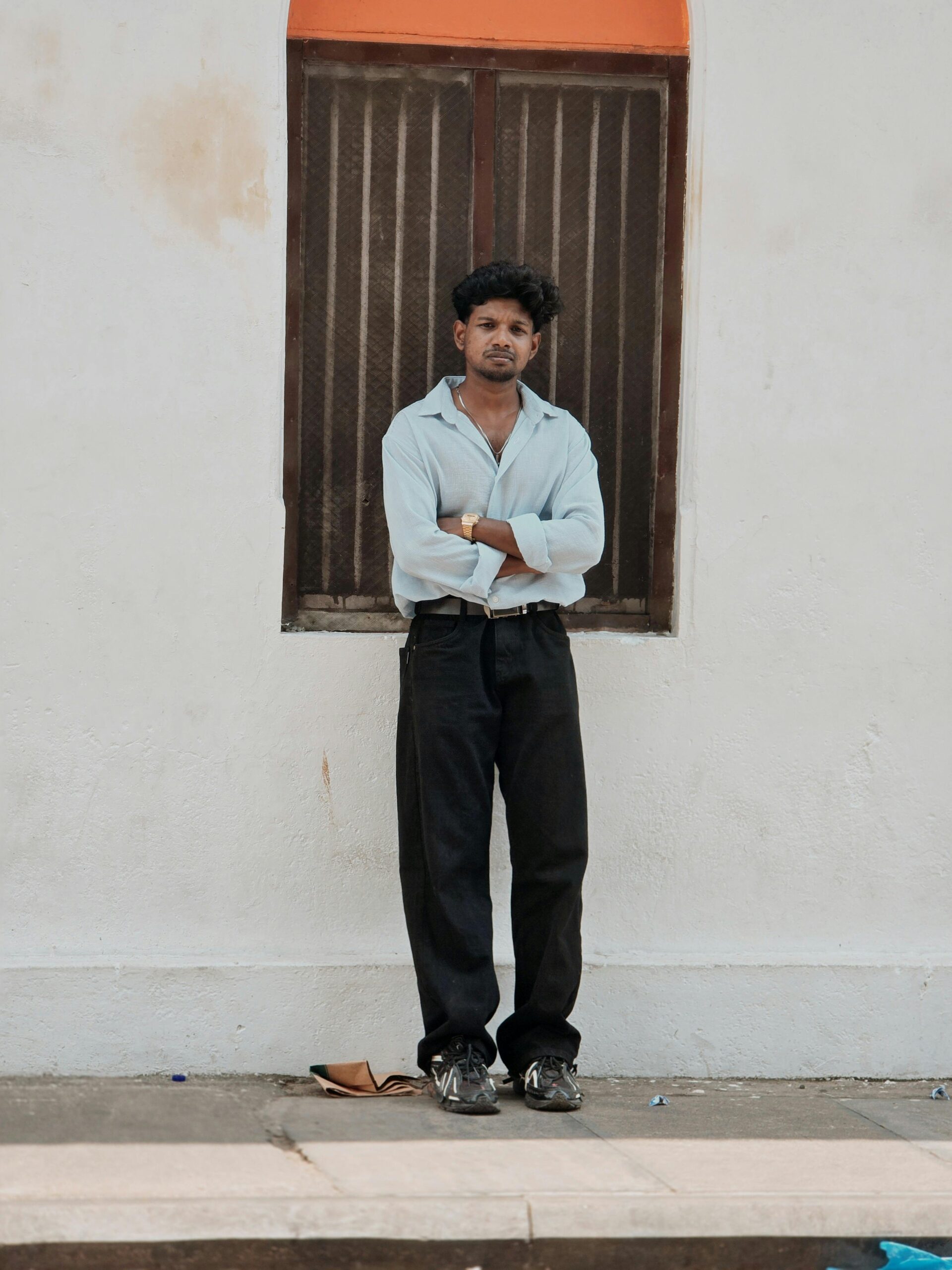 A man in casual attire stands by a window with calm expression, outdoors.